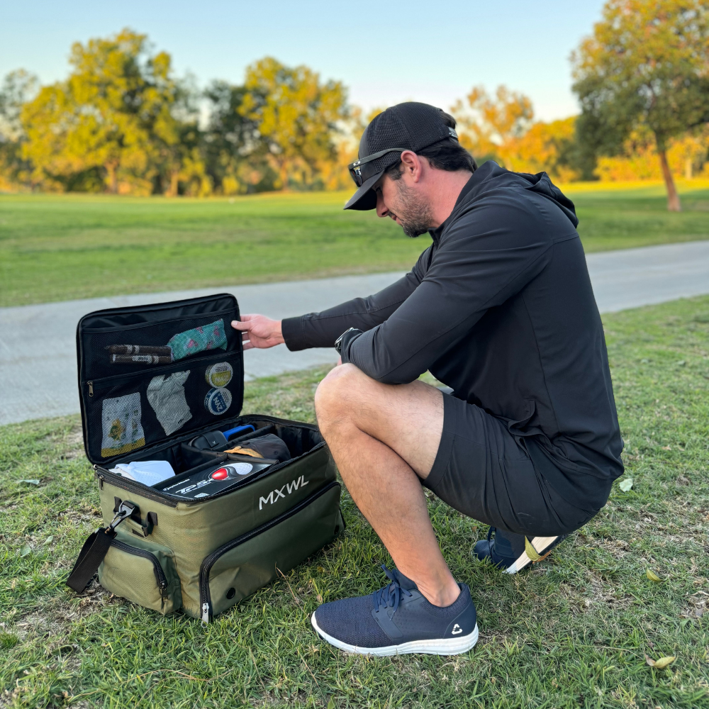 Man opening a green cooler bag labeled 'MXWL' in a park setting.