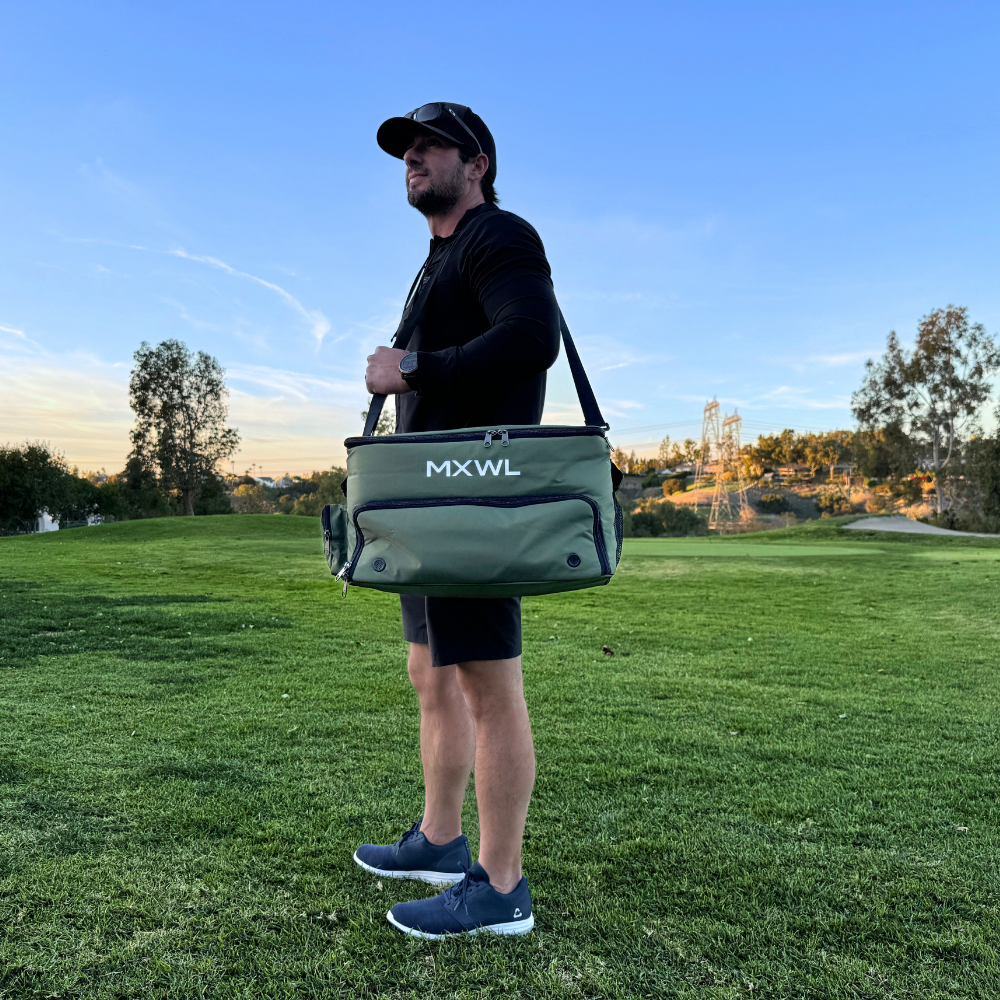Man holding a green bag with 'MXWL' branding on a grassy field.