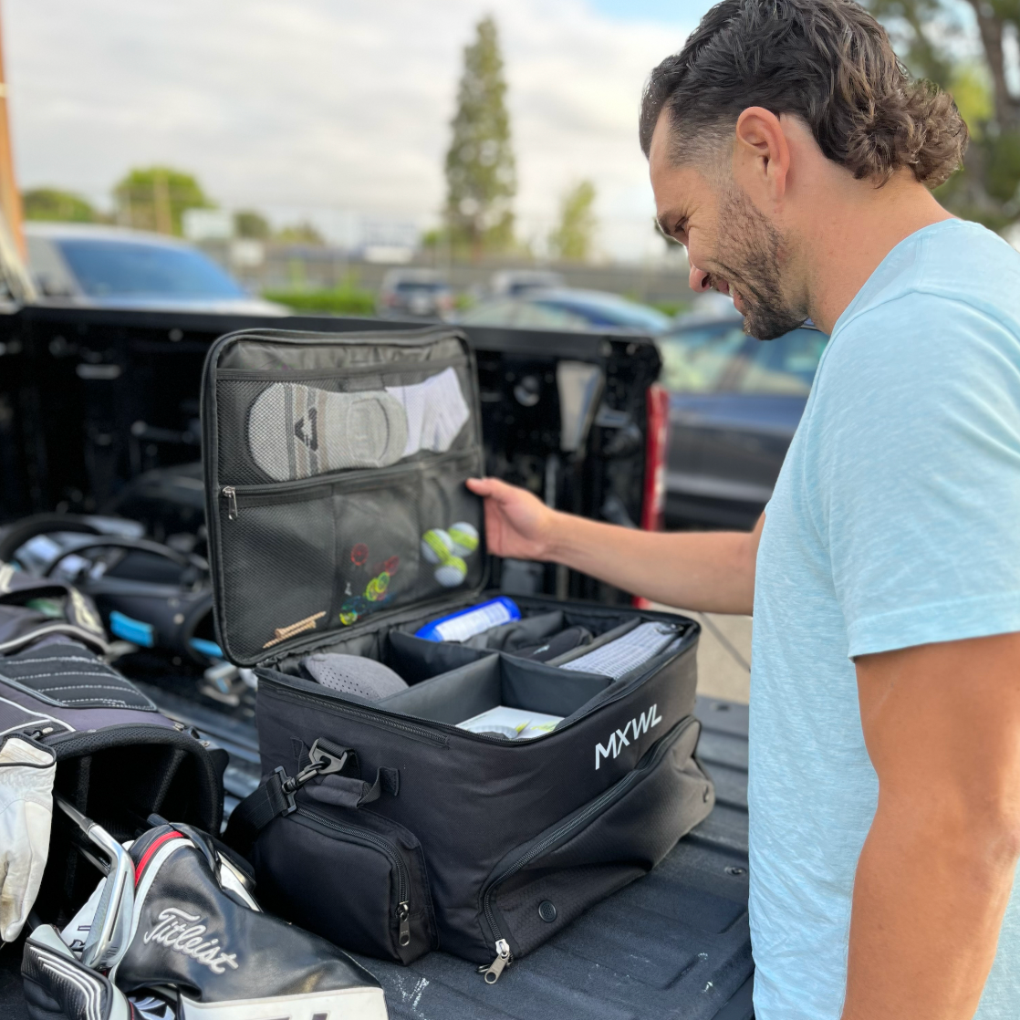 Man organizing golf equipment in a black bag on a truck bed.
