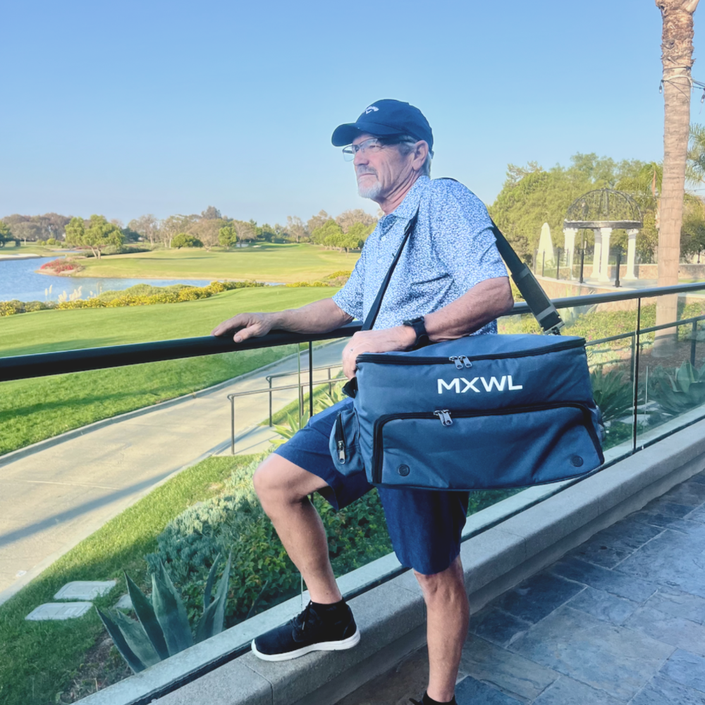 Man holding a blue cooler bag with 'MXWL' branding at a golf course.